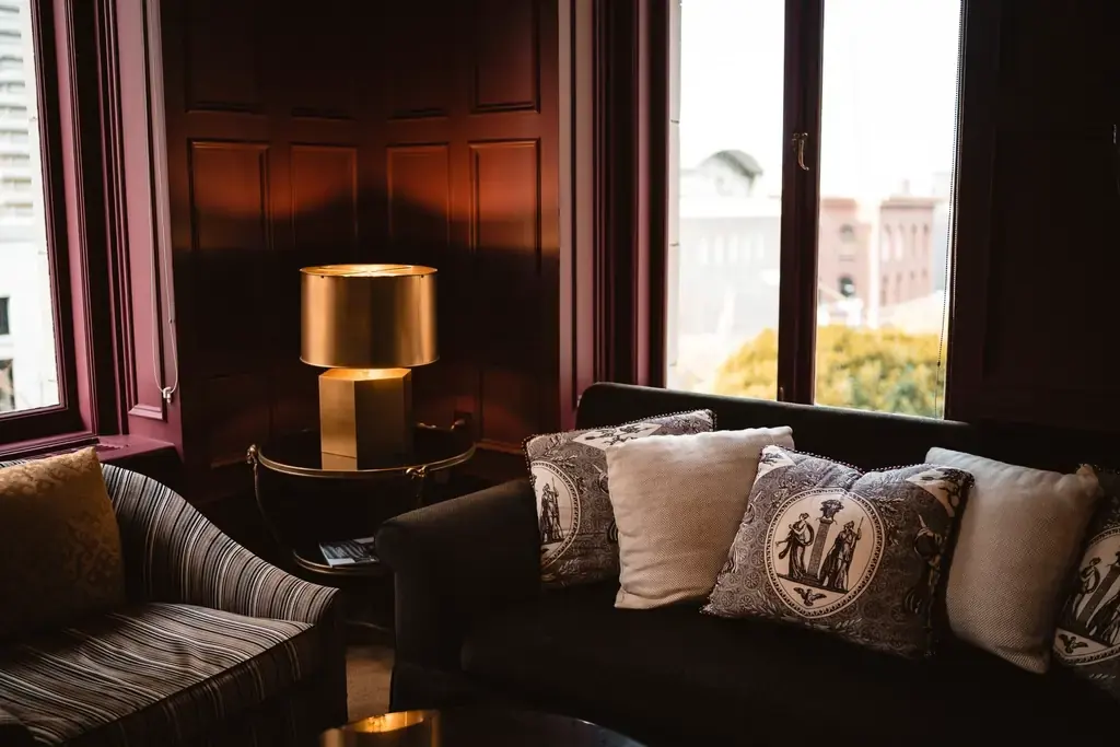 Oak-panelled lounge in warm evening light, with a brass table lamp and a deep sofa layered with patterned cushions