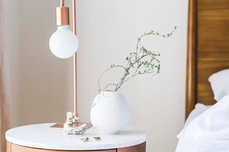 Marble side table with a glass globe lamp and a white vase holding a single branch